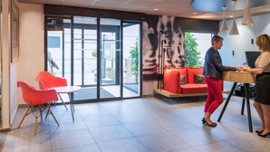 A modern lobby with a seating area, a reception desk, and a large glass door leading outside. - ibis Tours Nord (Tours)