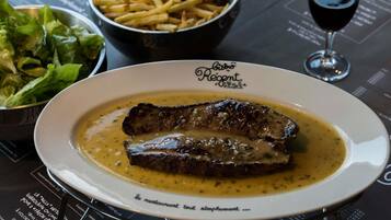 Un piatto di bistecca con salsa, una ciotola di patatine fritte, un bicchiere di vino rosso e un'insalata come contorno su un tavolo con un menu.