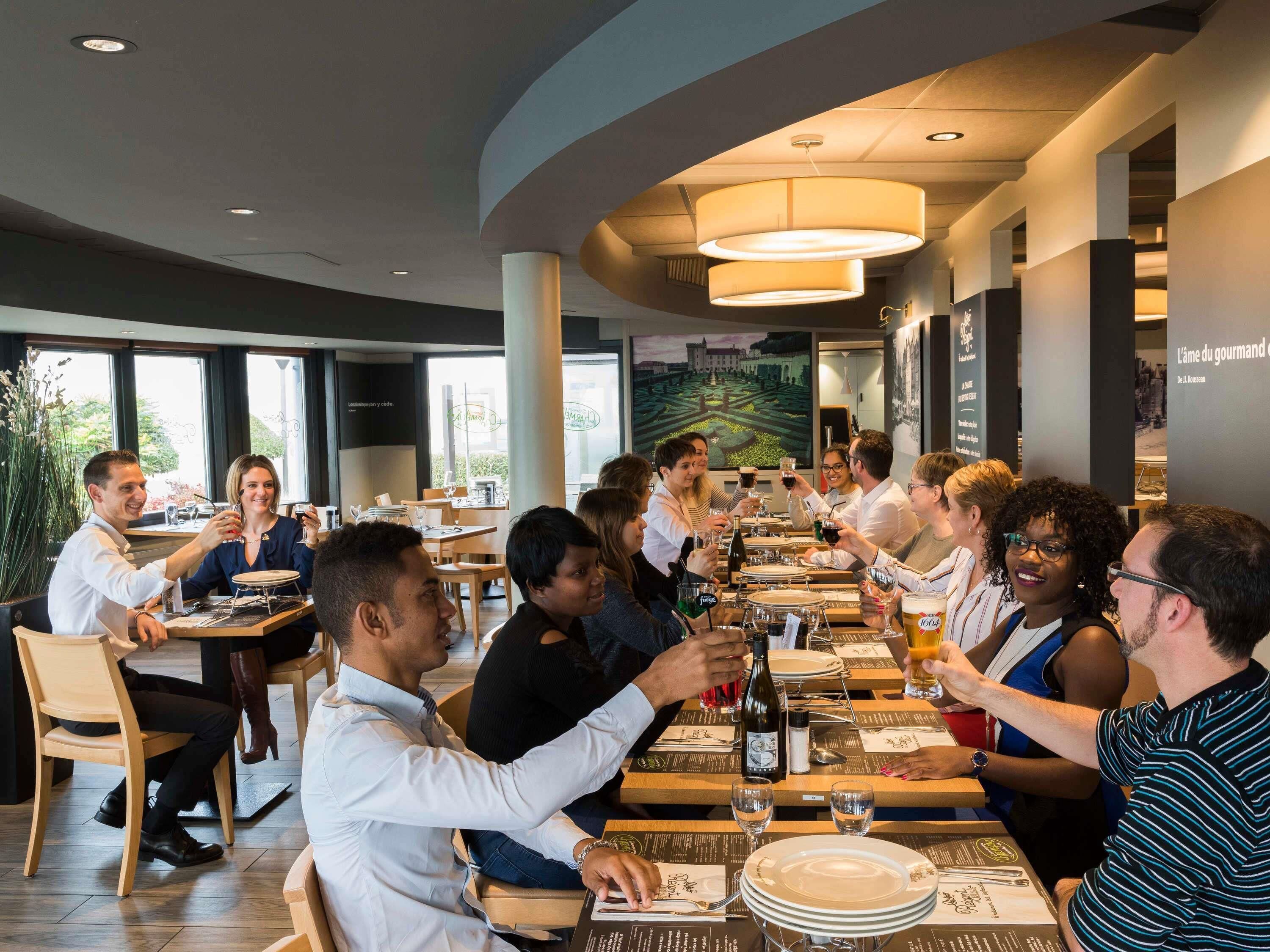 Een restaurant met ronde tafels, mensen aan het dineren en een groot raam met uitzicht.