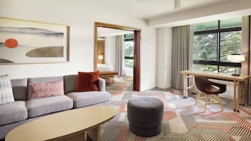 A modern hotel room with a sofa, ottoman, desk, and a large window with a view.