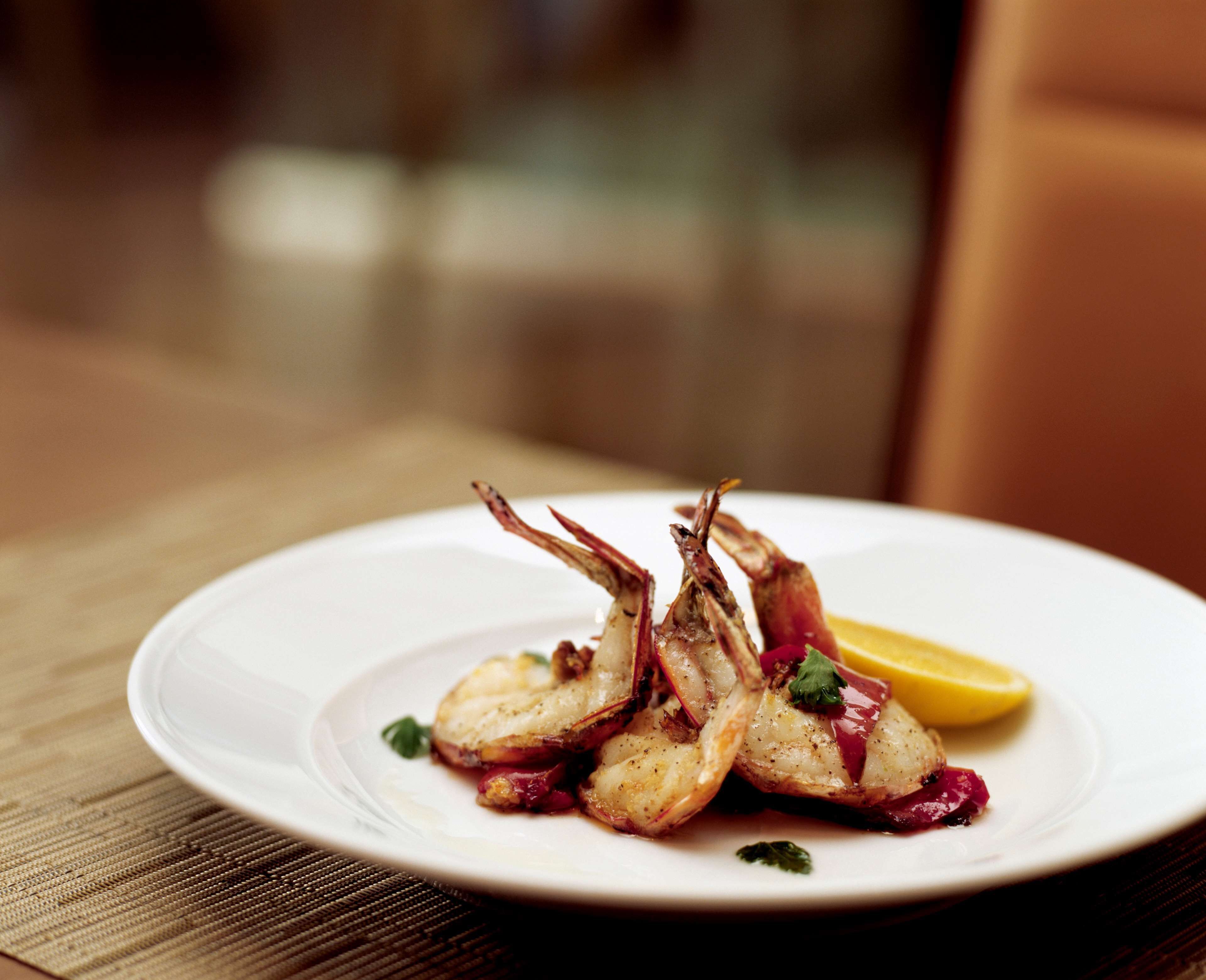 A plate of cooked seafood, possibly shrimp, with a lemon wedge on a white plate.