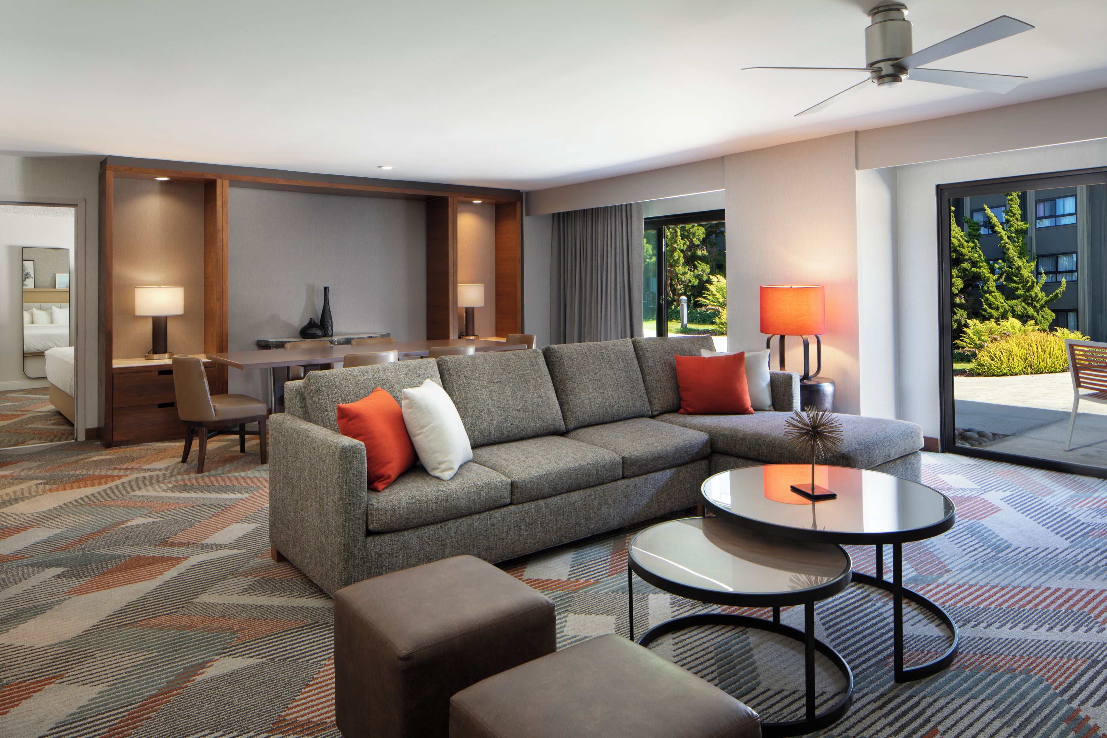Een moderne hotelkamer met een bank, fauteuils, een eettafel en een plafondventilator.