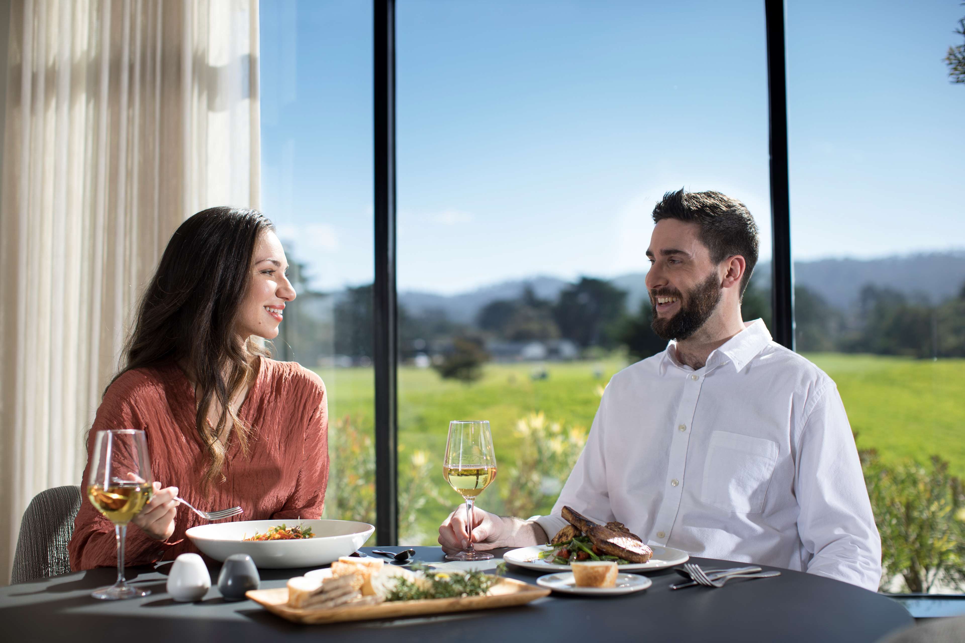 Une table à manger donnant sur un paysage verdoyant grâce à de grandes fenêtres.