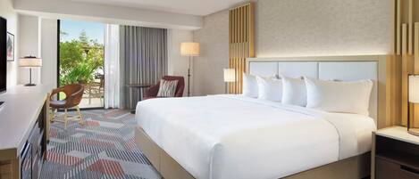 Habitación de hotel con una cama grande, un escritorio, una silla, un televisor y vistas al exterior.
