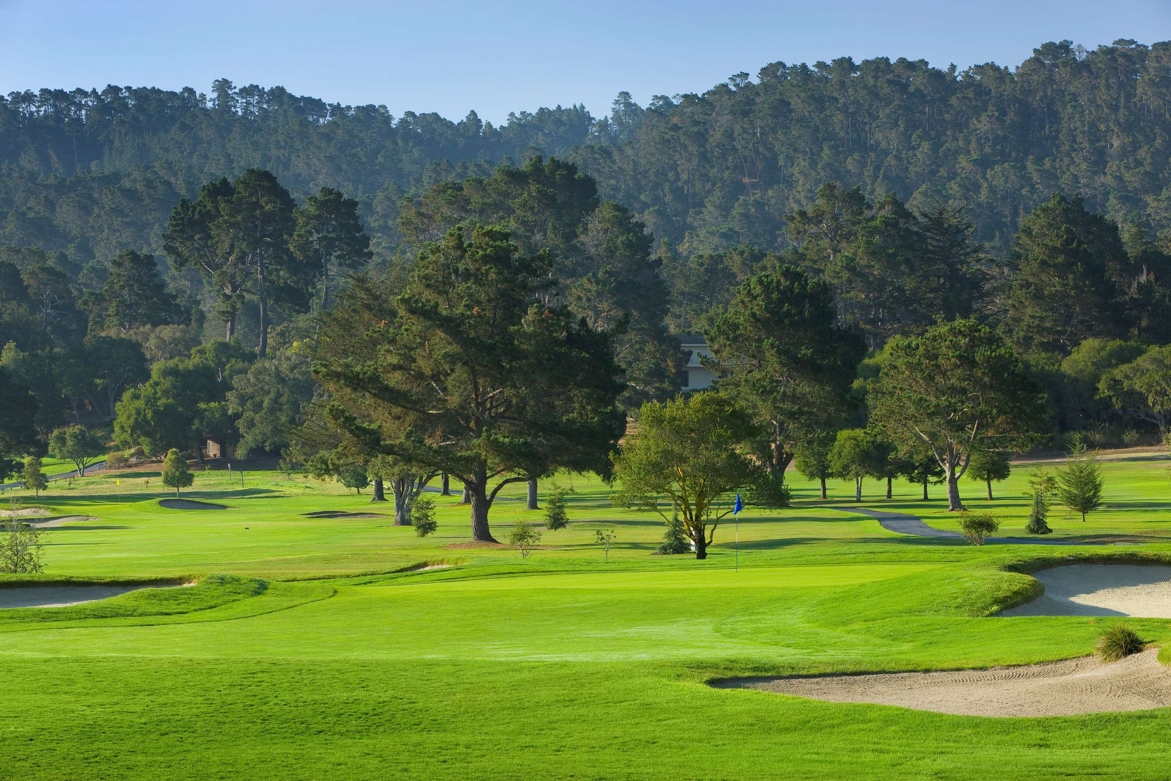 Un campo de golf con búnkeres de arena, árboles y un paisaje montañoso.