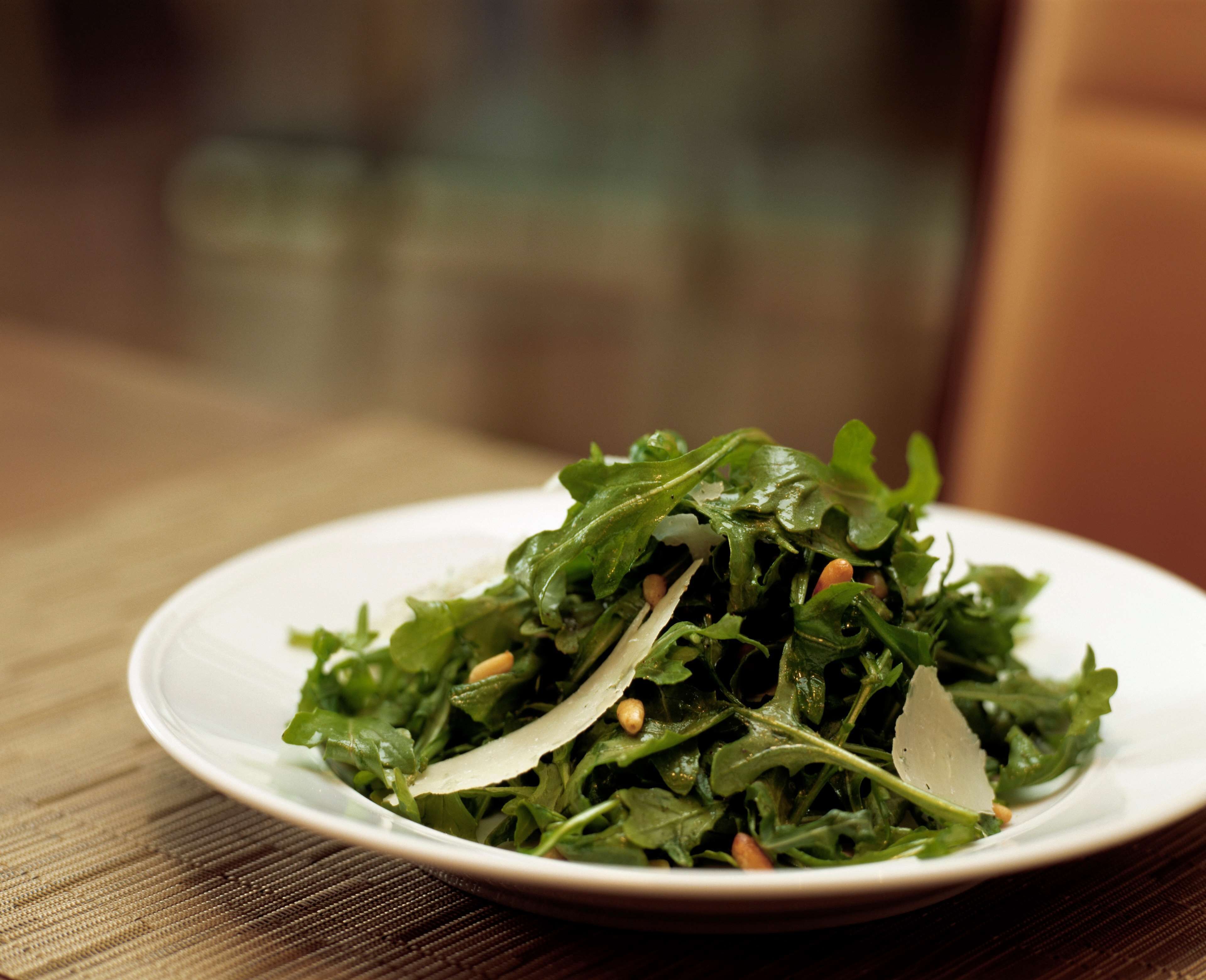 Une assiette de salade de roquette, agrémentée de pignons de pin et de copeaux de parmesan, servie sur une assiette blanche.