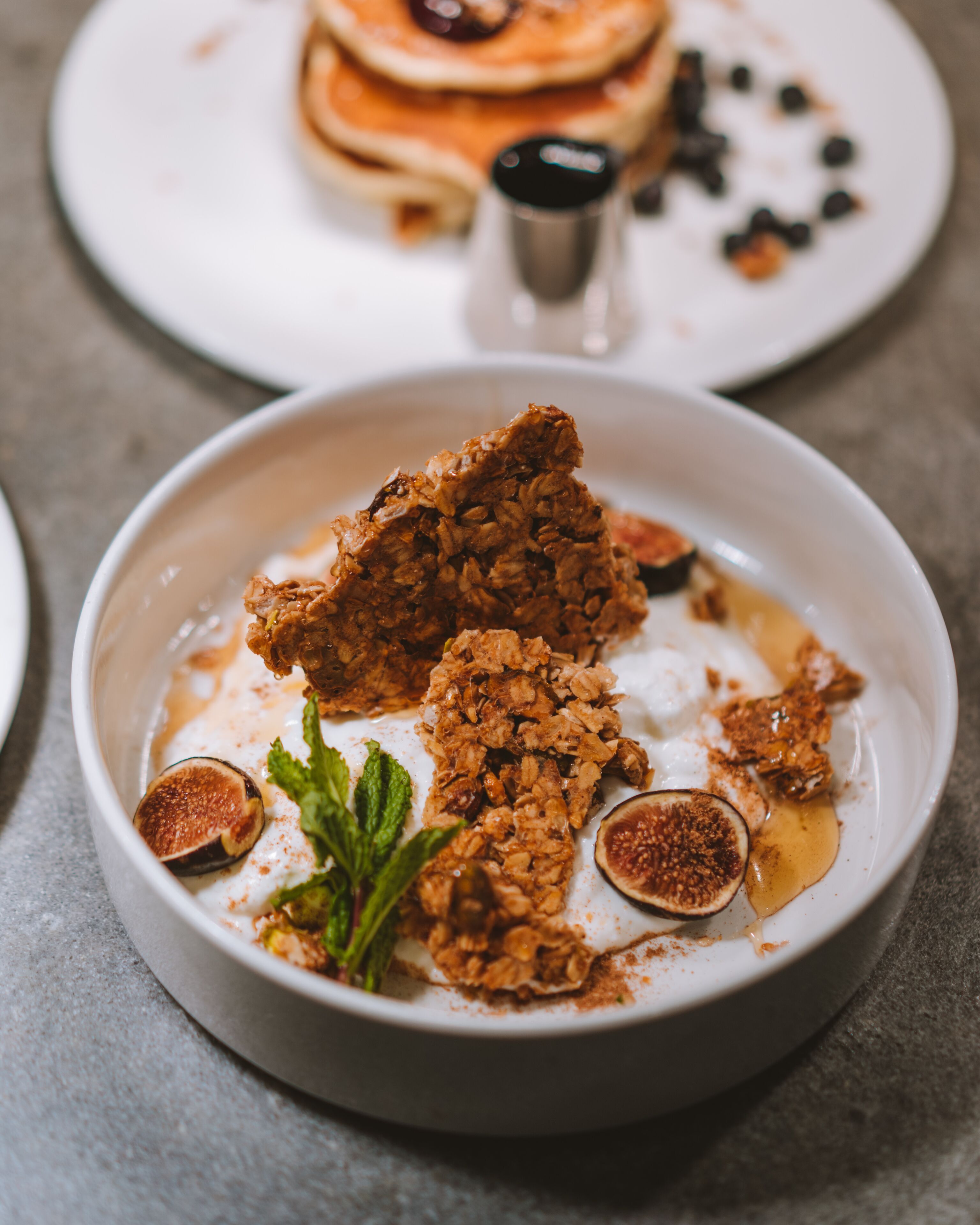 Une assiette de dessert garnie de granola, de figues et de quelques feuilles de menthe.