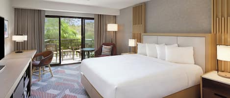 Ein Hotelzimmer mit einem großen Bett, einem Schreibtisch, einem Sessel und einem Balkon mit Tisch, sowie einem Deckenventilator.