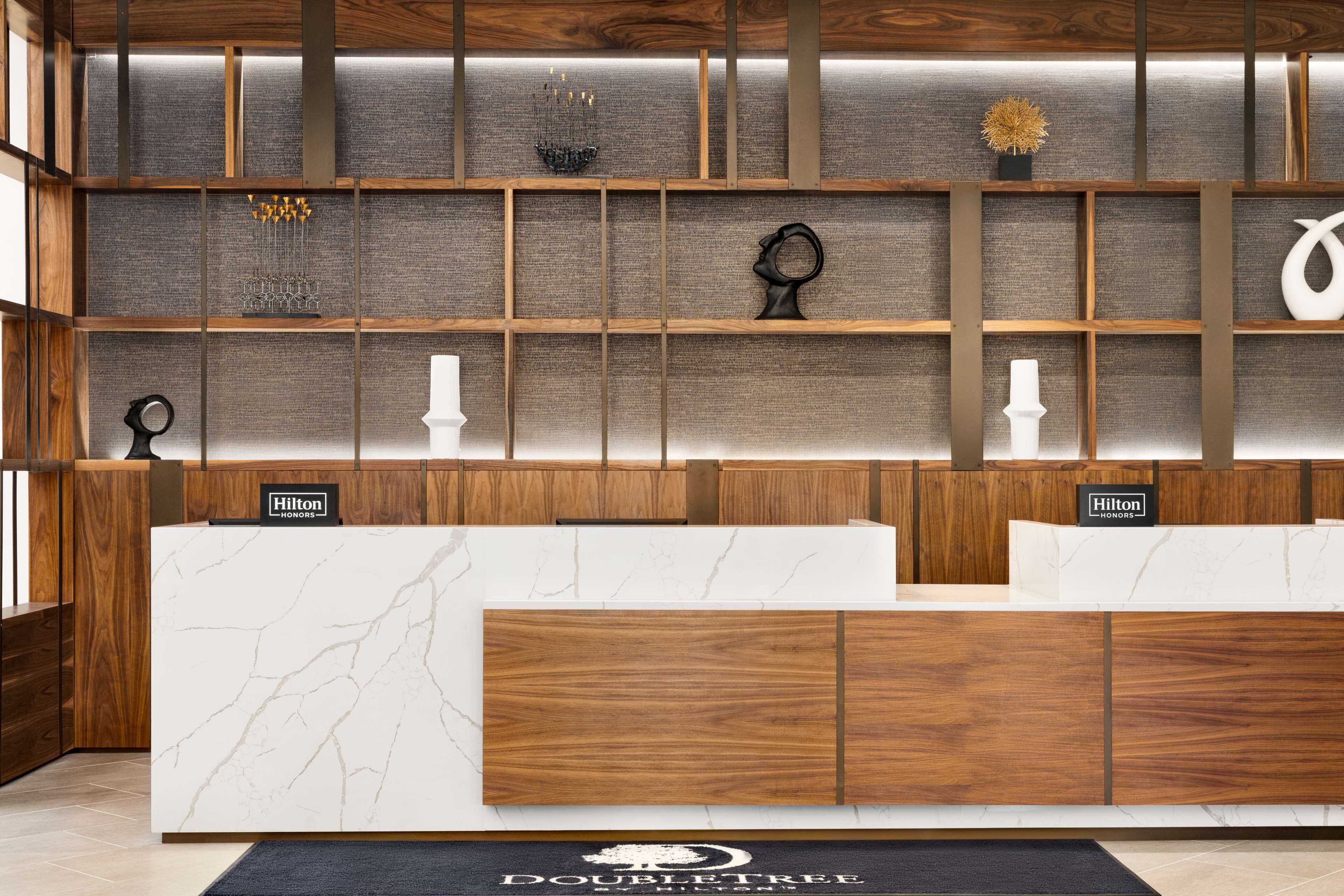 A reception desk with a marble top and wooden paneling, a "Hilton Honors" sign, and a "DoubleTree" logo on the floor.