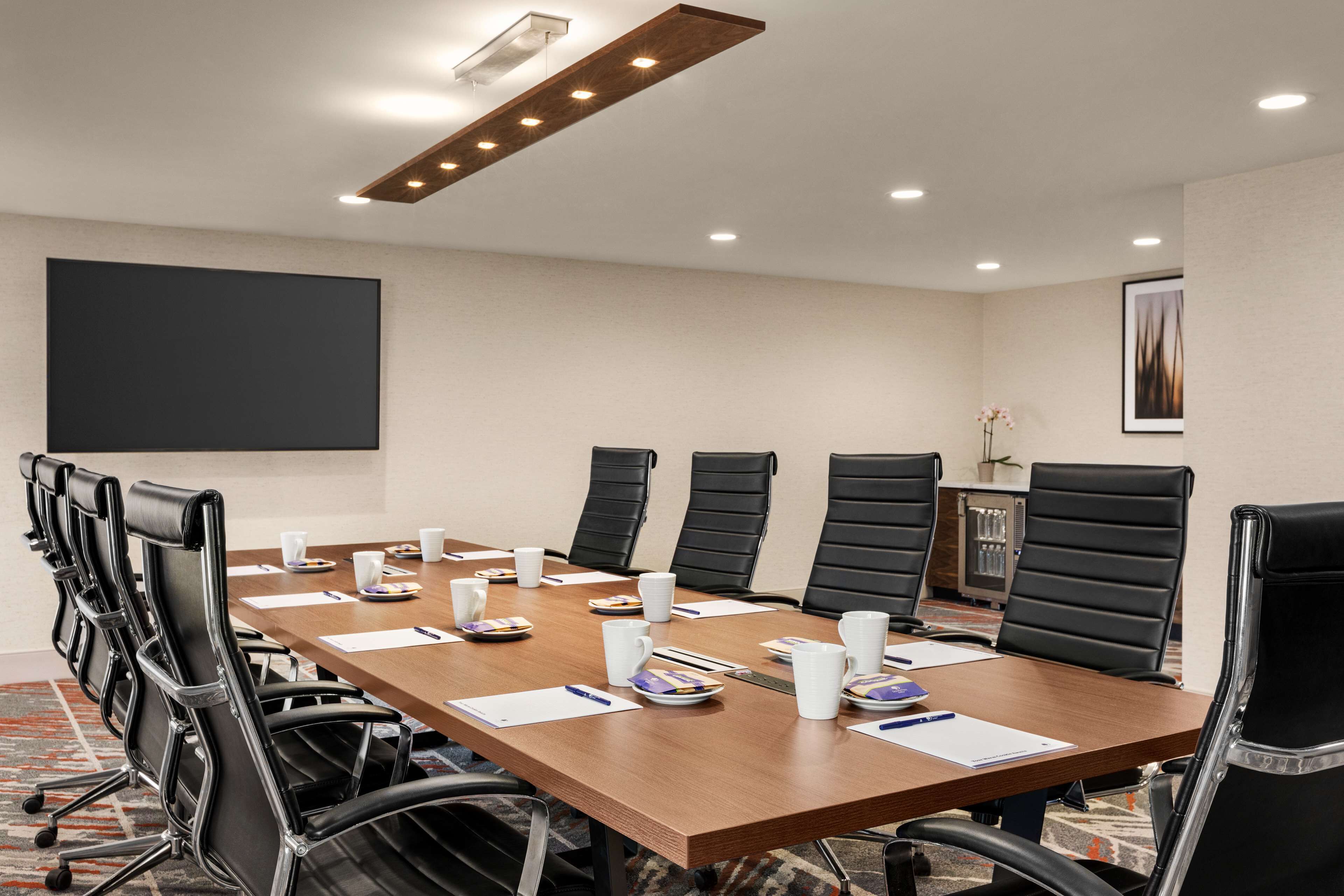 Une salle de conférence avec une longue table, des chaises noires, des tasses blanches et des documents.