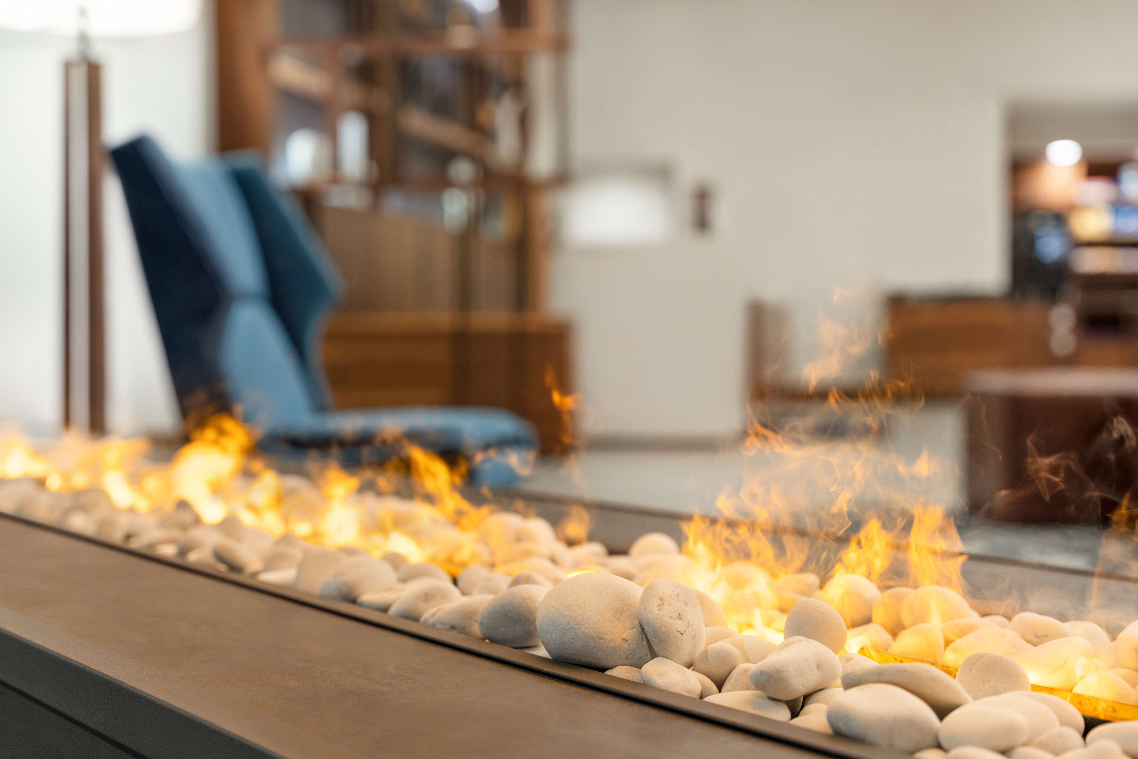 A fire feature with white stones and flames, a blue chair, and a wooden table in the background.