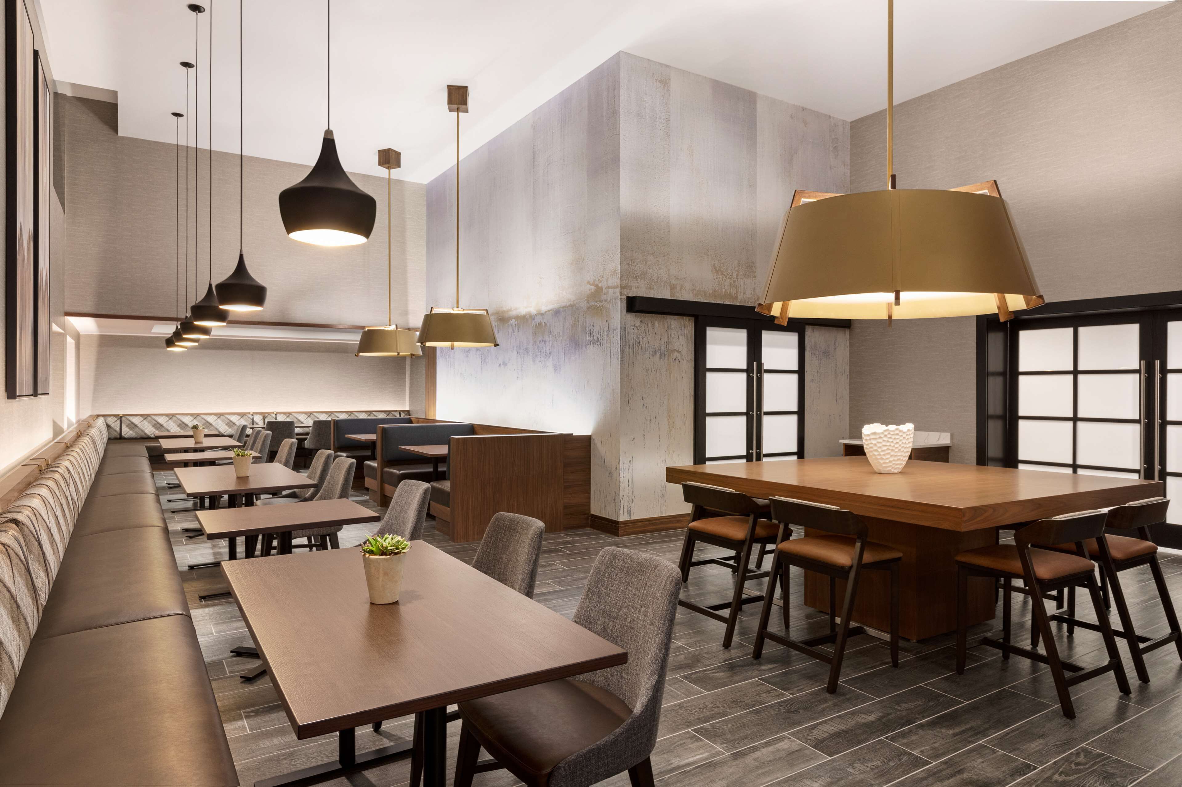 A modern restaurant with long communal tables and booths, pendant lighting, and a neutral color palette.