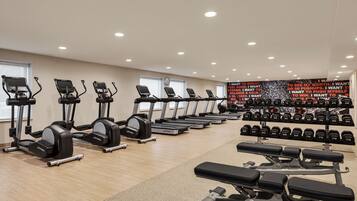A gym with treadmills, elliptical machines, dumbbells, and weight benches.