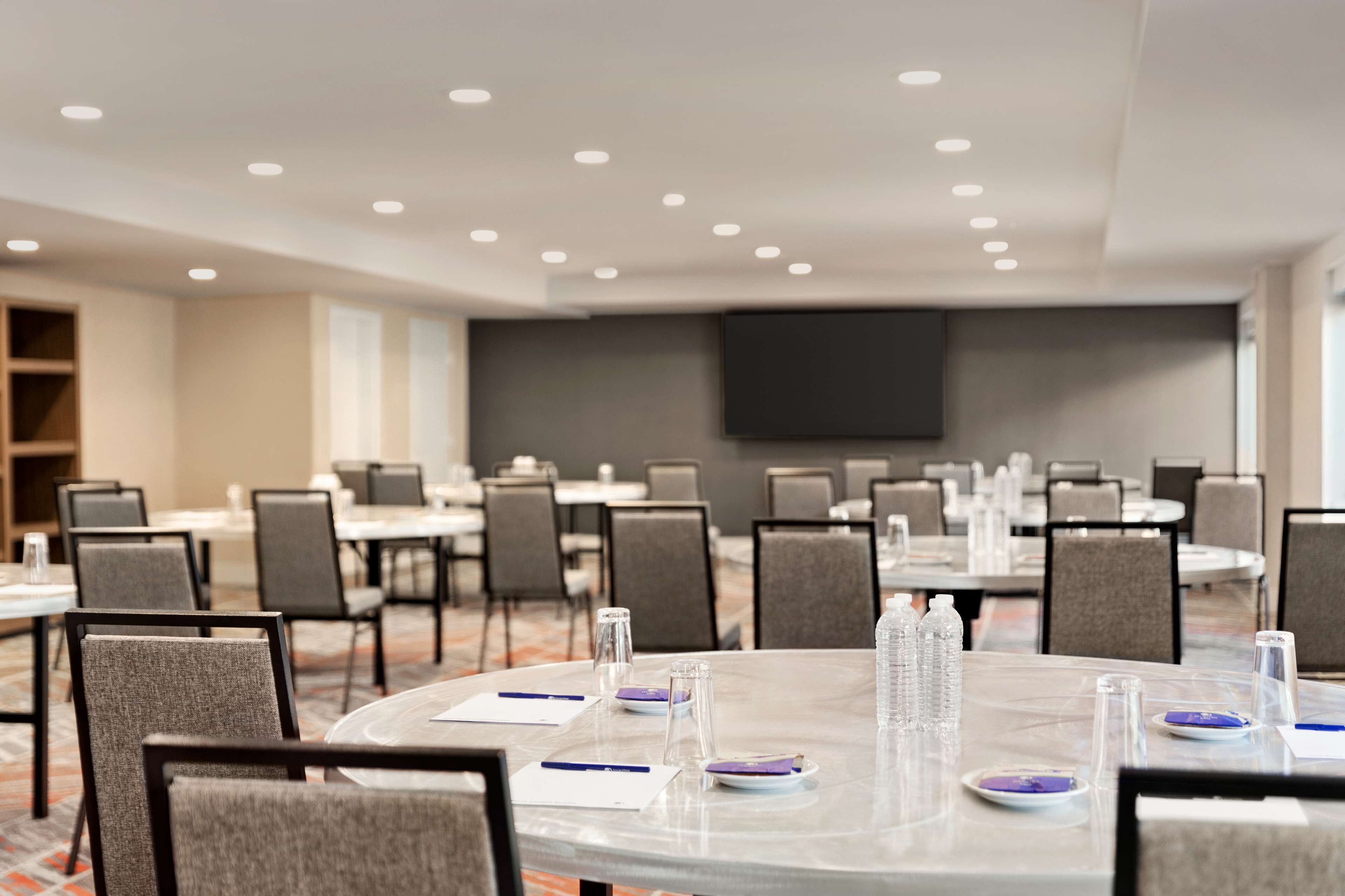 A conference room with round tables, chairs, and a large screen.