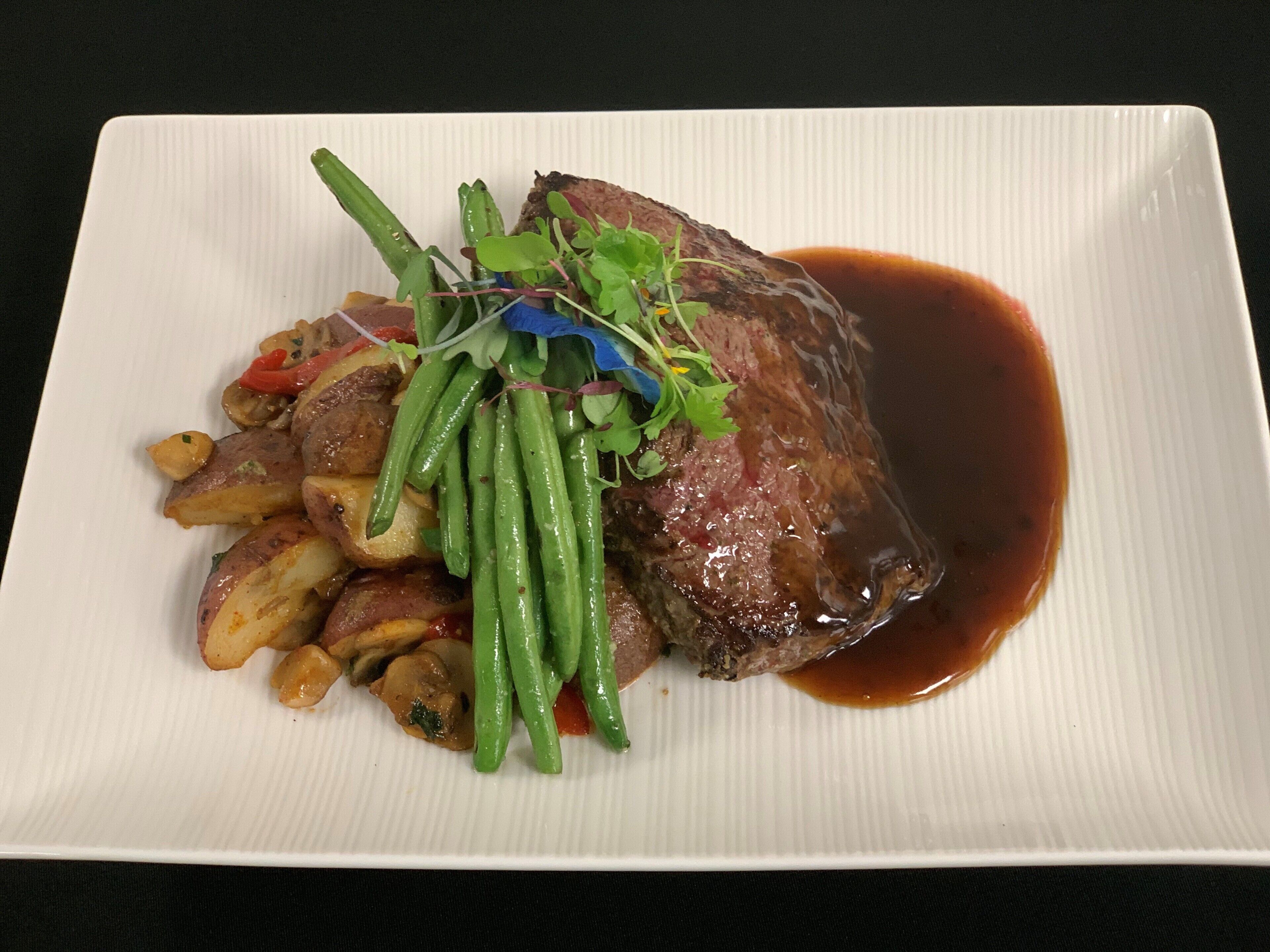 A plate with a steak, green beans, and roasted potatoes.