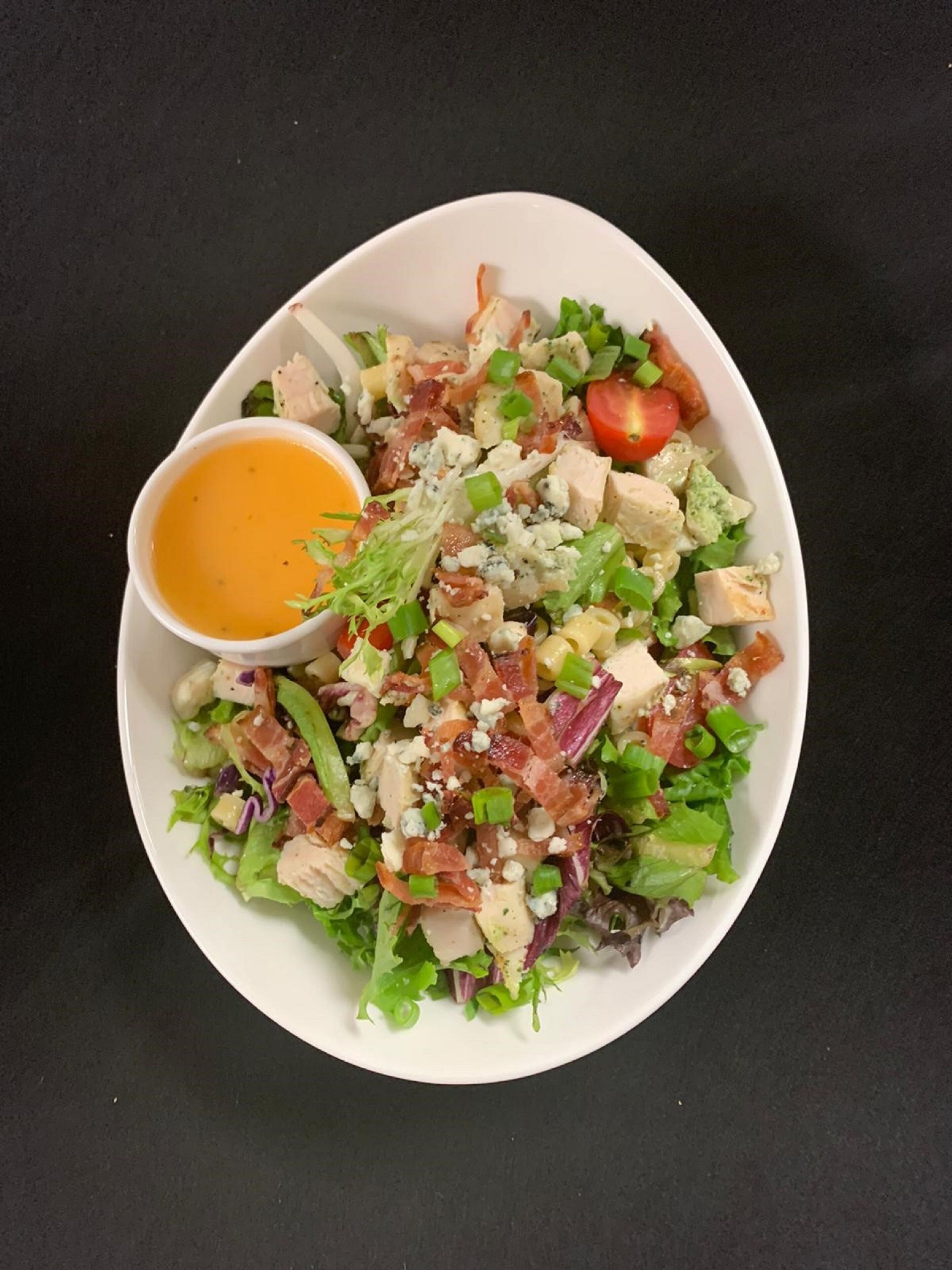 Un tazón blanco con una ensalada de diversos ingredientes y una taza pequeña de aderezo.