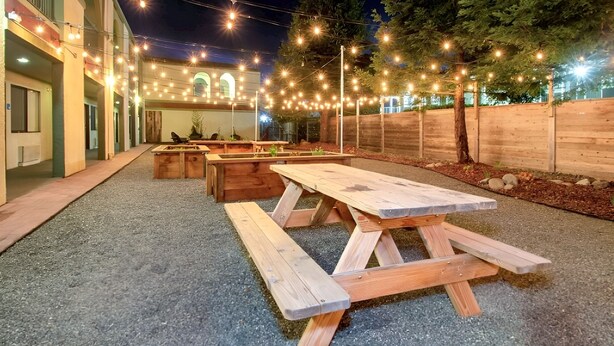 Un espace extérieur aménagé en terrasse, avec des tables de pique-nique en bois et des guirlandes lumineuses.