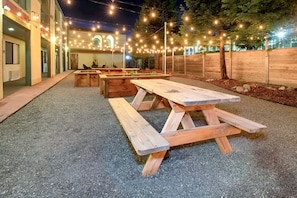 An outdoor patio area with wooden picnic tables and string lights. - The Redwood Riverwalk, A Boutique Hotel (Fortuna)