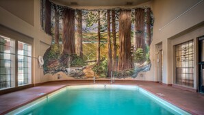 Une piscine dont le mur, au-dessus, est décoré d’une fresque représentant une scène de forêt.