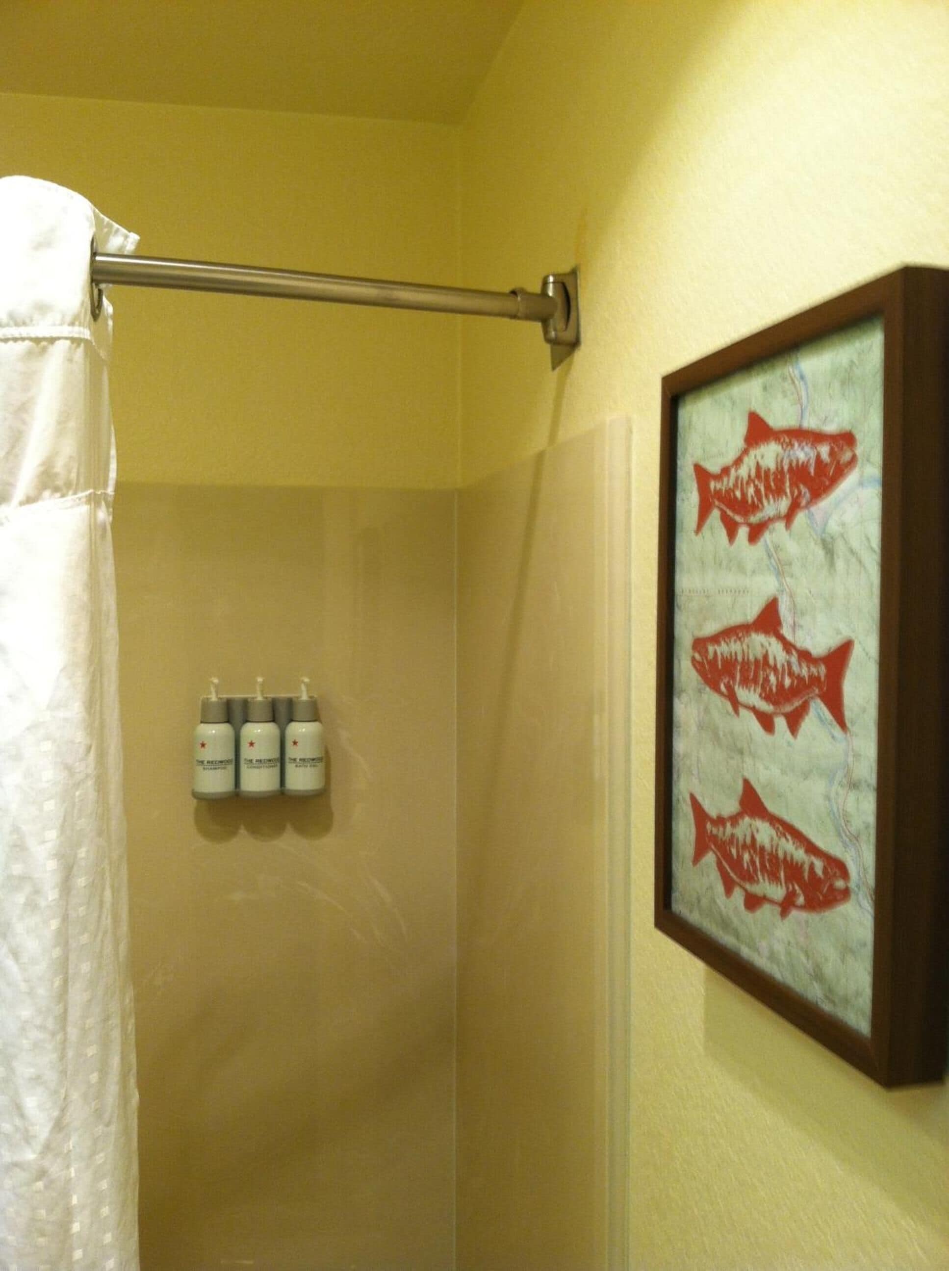 A bathroom with a shower curtain, a towel rack, and a framed fish painting on the wall.