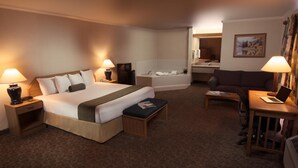Une chambre d’hôtel avec un lit, des tables de chevet, un bureau avec un ordinateur portable, une chaise, un canapé et une salle de bain visible au fond.
