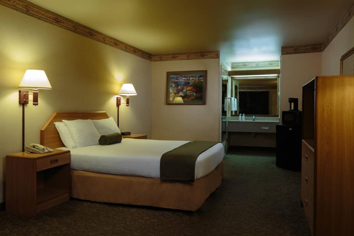 A hotel room with a bed, bedside lamps, a painting, a mirror, and a dresser.