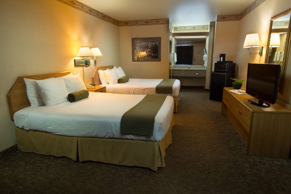 A hotel room with two beds, a desk, a television, and a mirror.
