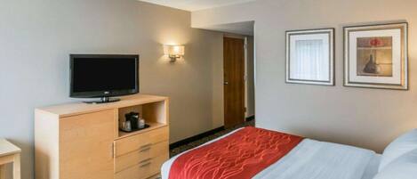 A hotel room with a bed, a TV on a wooden dresser, a hallway, and two framed pictures on the wall.