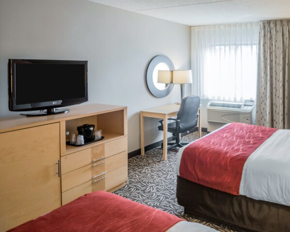 A hotel room with a TV, a desk, a chair, and two beds.