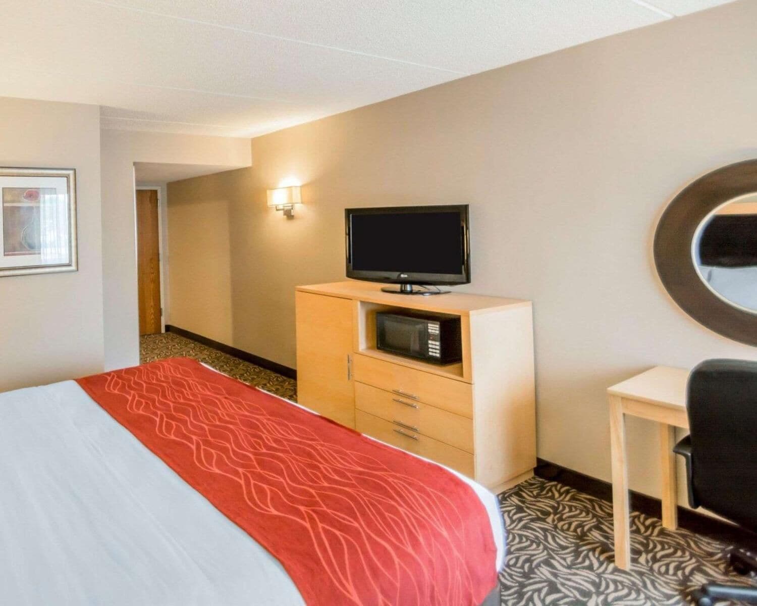 Camera d'albergo con un letto, una televisione su un mobile in legno, un forno a microonde, una scrivania e uno specchio.