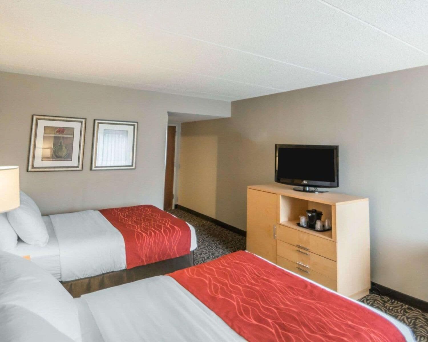 A hotel room with two beds, a TV on a wooden cabinet, and framed pictures on the wall.