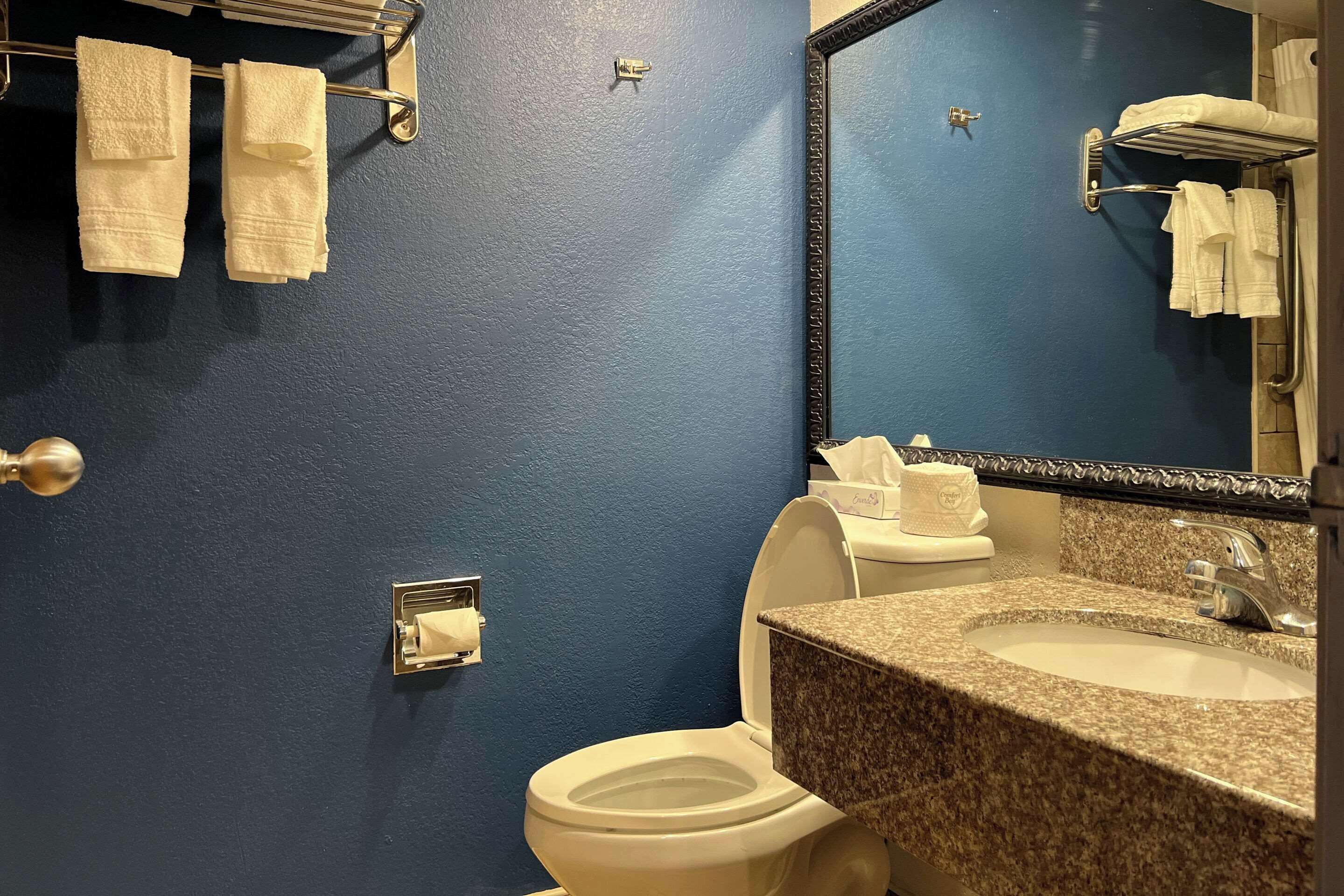 A bathroom with a blue wall, a white toilet, a granite sink, and a mirror with a towel rack above it.