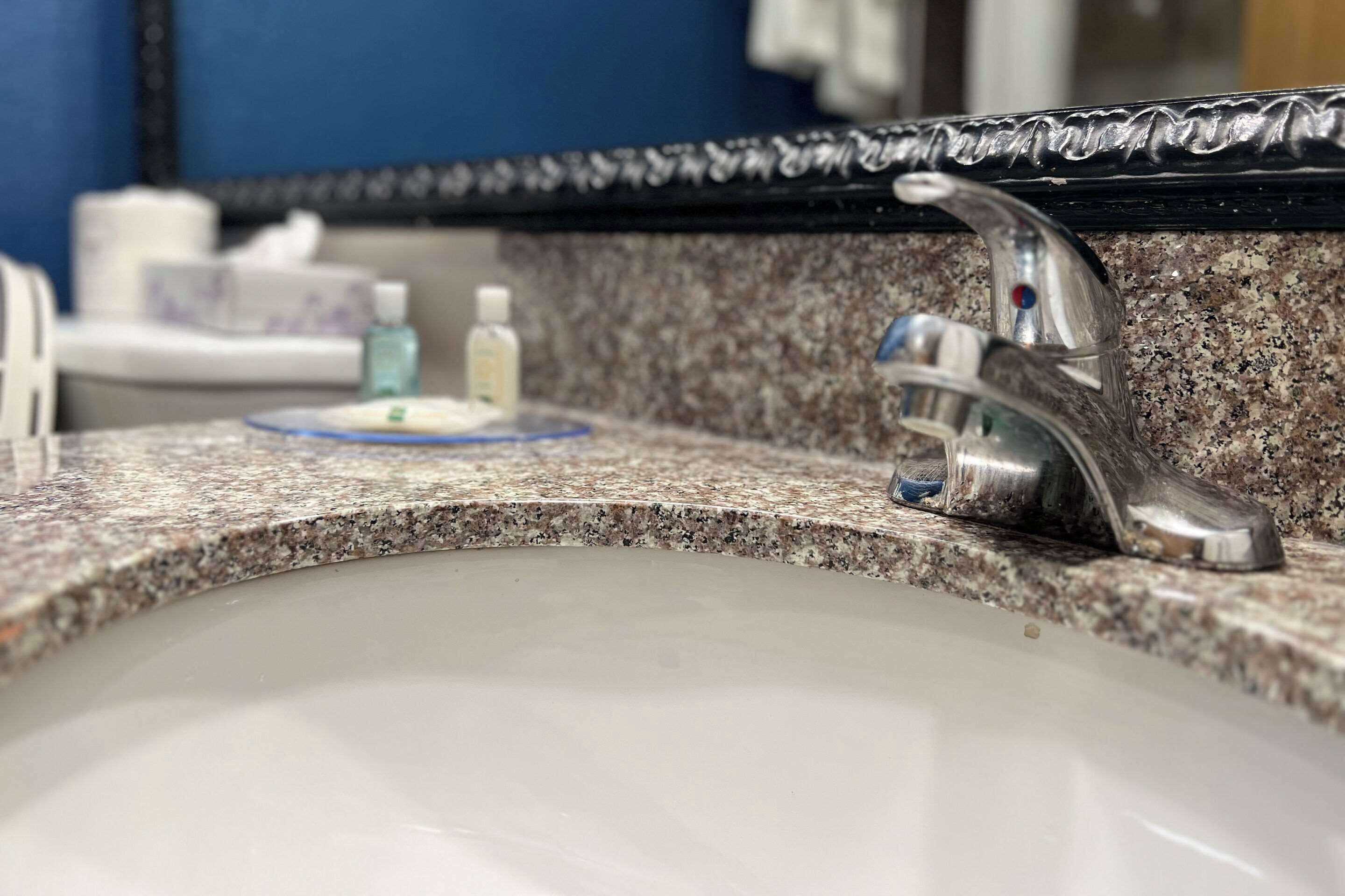 A bathroom sink with a granite countertop, a silver faucet, and a mirror above.