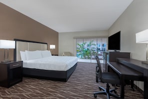 Quarto de hotel com cama, escrivaninha, cadeira, televisão e vista para o exterior.