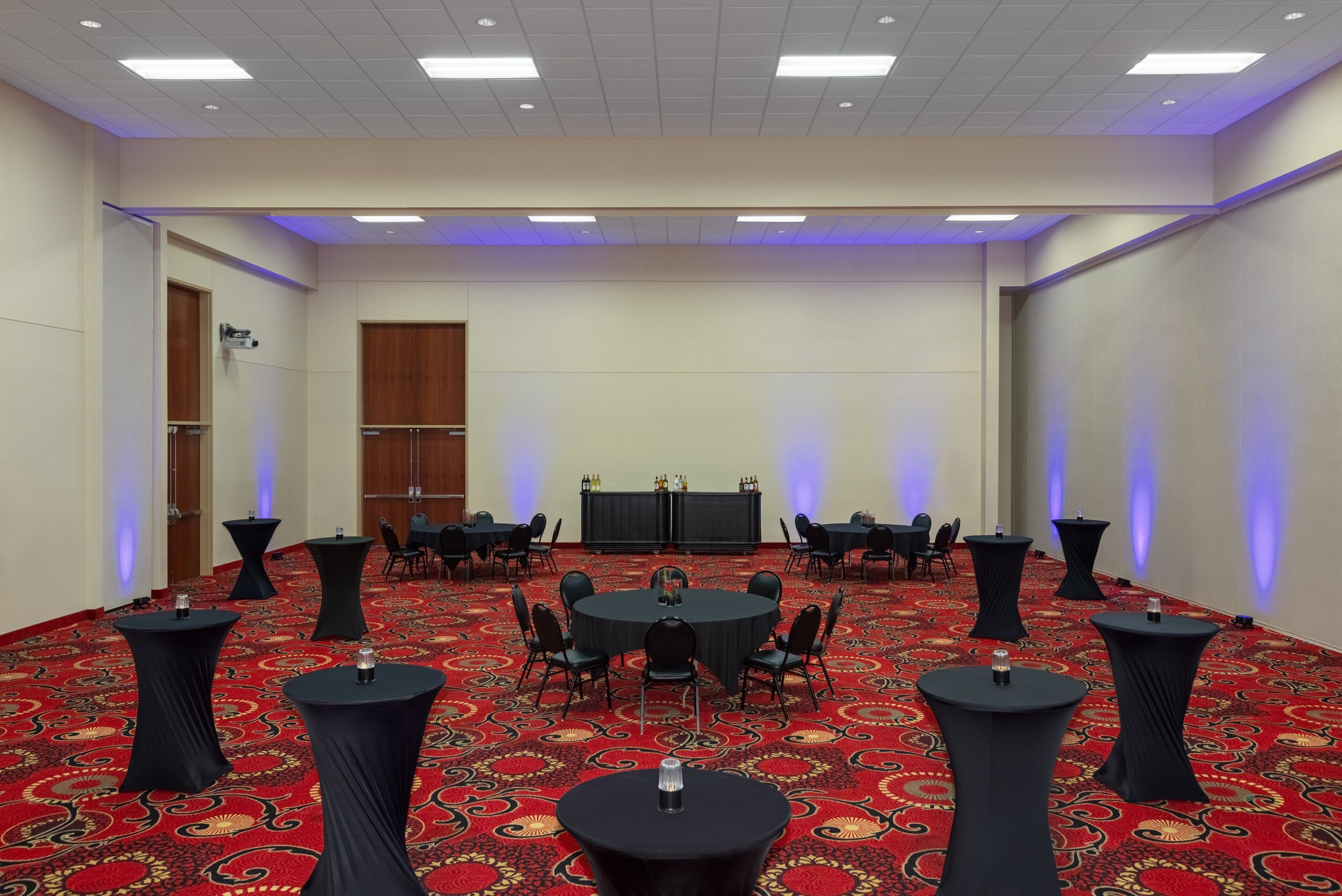 A conference room with a red carpet, round tables with chairs, and a stage with a podium.