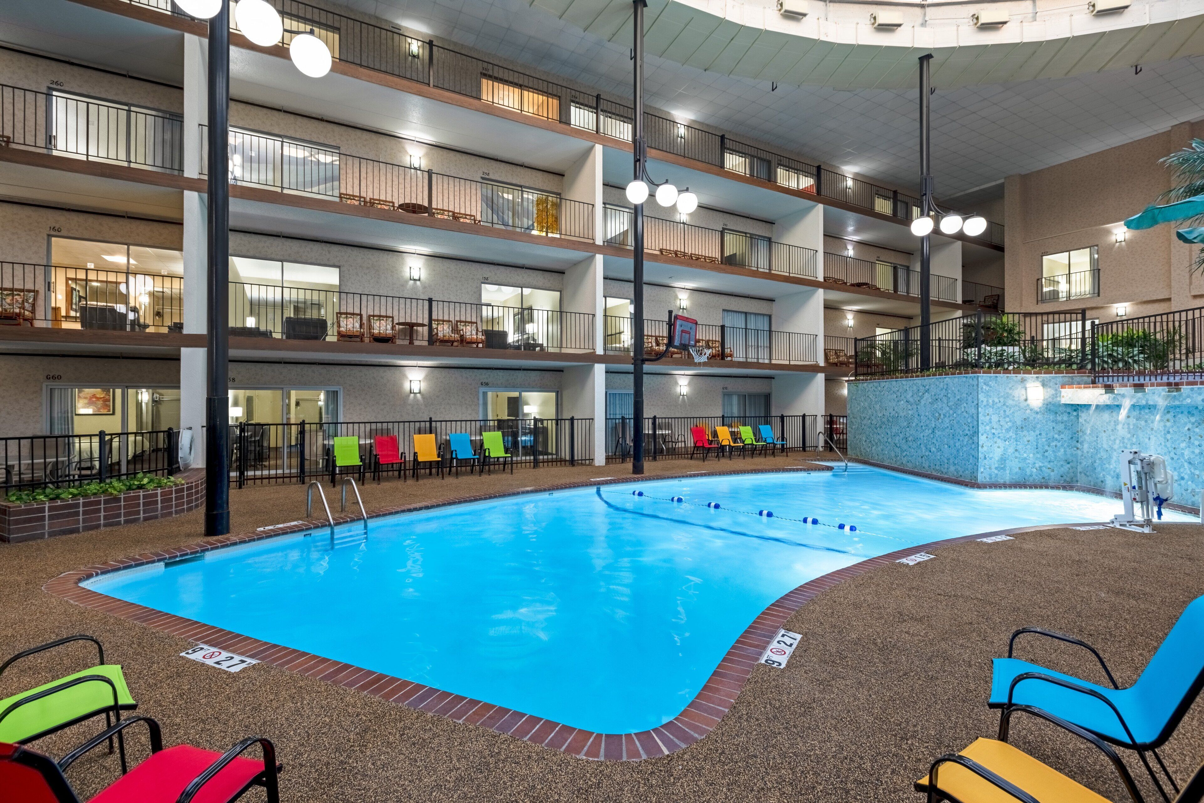 A multi-level indoor pool with a clear blue pool, multiple floors with balconies, and colorful lounge chairs.