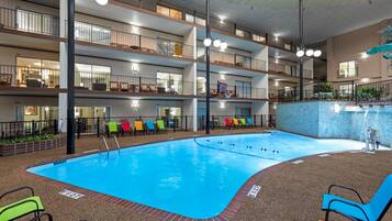 A multi-level indoor pool with a clear blue pool, multiple floors with balconies, and colorful lounge chairs.