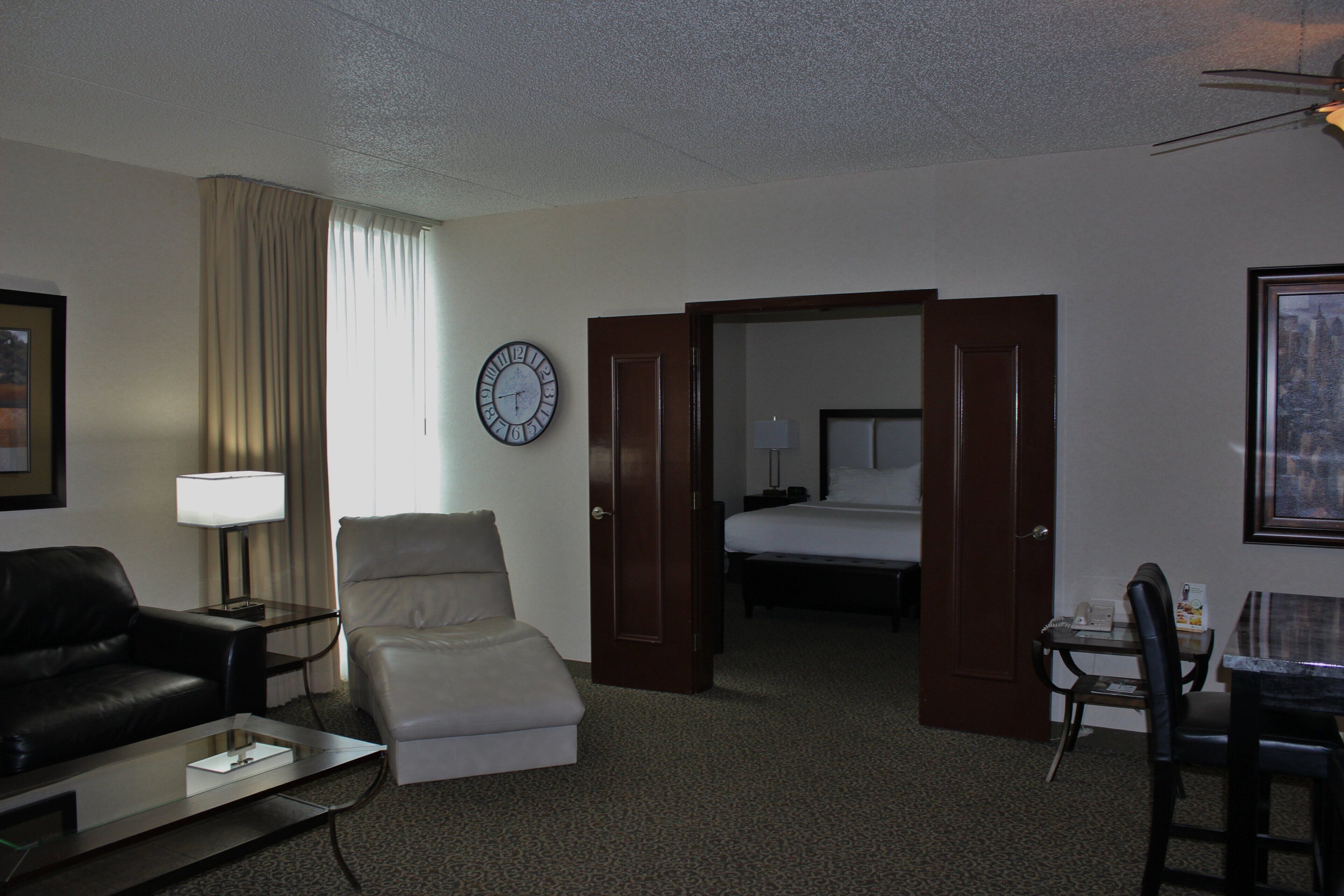 Una habitación de hotel con una cama, un escritorio con lámpara, un sillón de cuero, un sofá y un reloj en la pared.