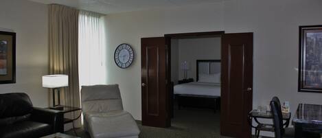 Una habitación de hotel con una cama, un escritorio con lámpara, un sillón de cuero, un sofá y un reloj en la pared.