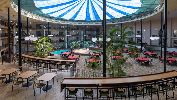 A spacious indoor area with multiple levels, featuring a central open space with tables and chairs, surrounded by balconies and a large, colorful ceiling structure. - Holiday Inn Des Moines-Airport/Conf Center by IHG (Des Moines)