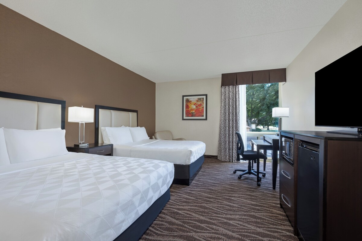 Quarto de hotel com duas camas, uma escrivaninha, uma televisão e uma janela com cortinas.