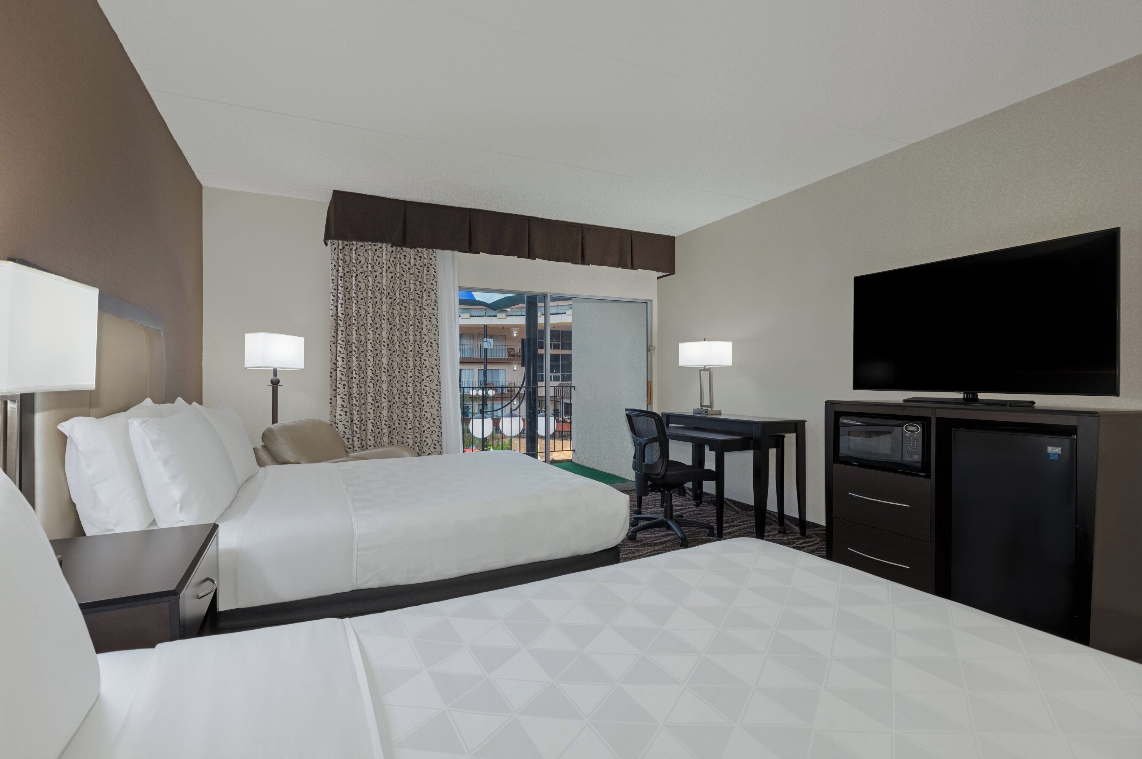 A hotel room with two beds, a desk, a television, and a minibar.