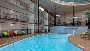 A multi-level indoor swimming pool with a clear water surface, surrounded by colorful lounge chairs and a stone wall. - Holiday Inn Des Moines-Airport/Conf Center by IHG (Des Moines)