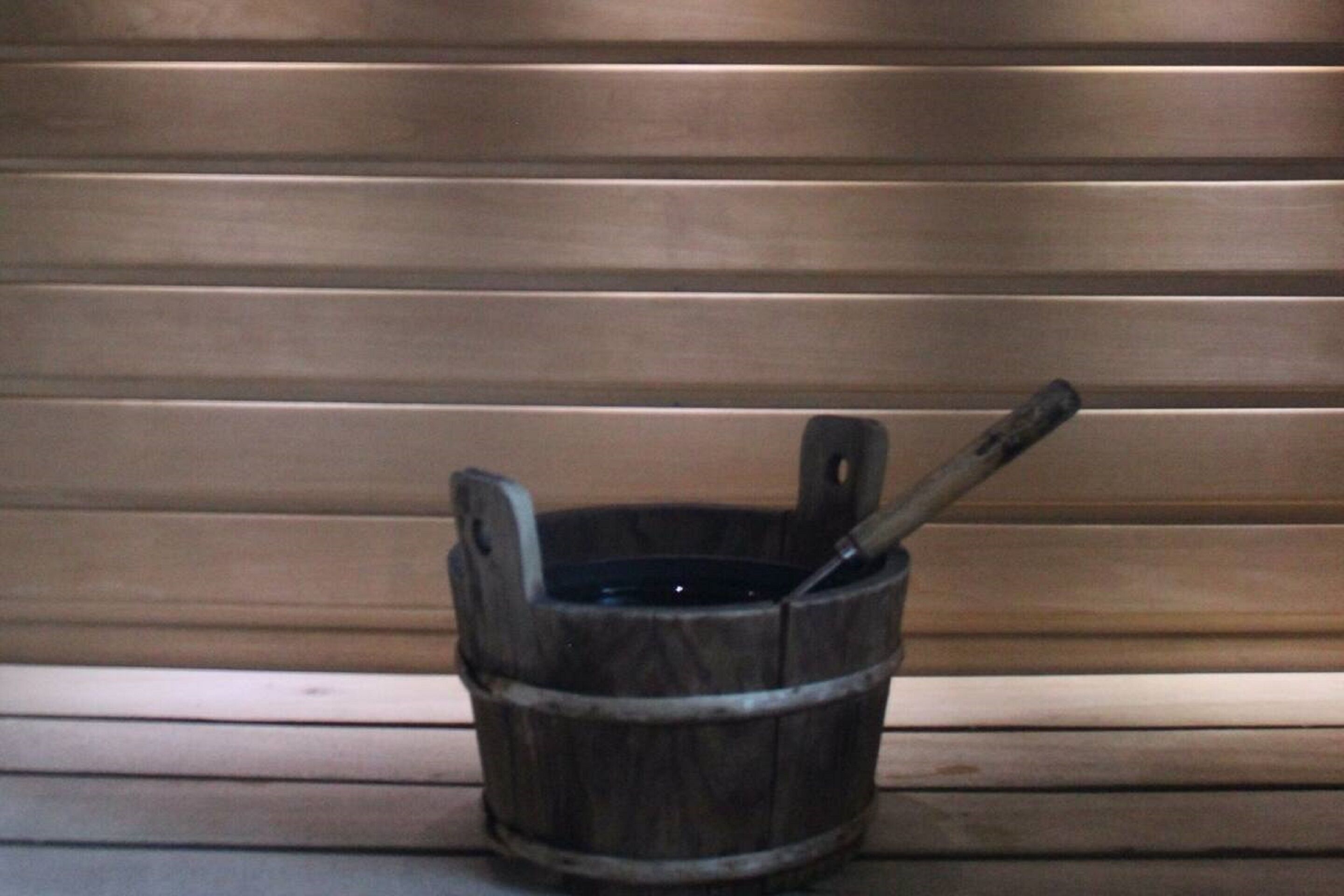 A wooden bucket with a metal handle and a metal scoop, placed on a wooden bench.