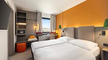 Ett hotellrum med två sängar, ett skrivbord, en stol, en liten orange pall och utsikt över omgivningarna.