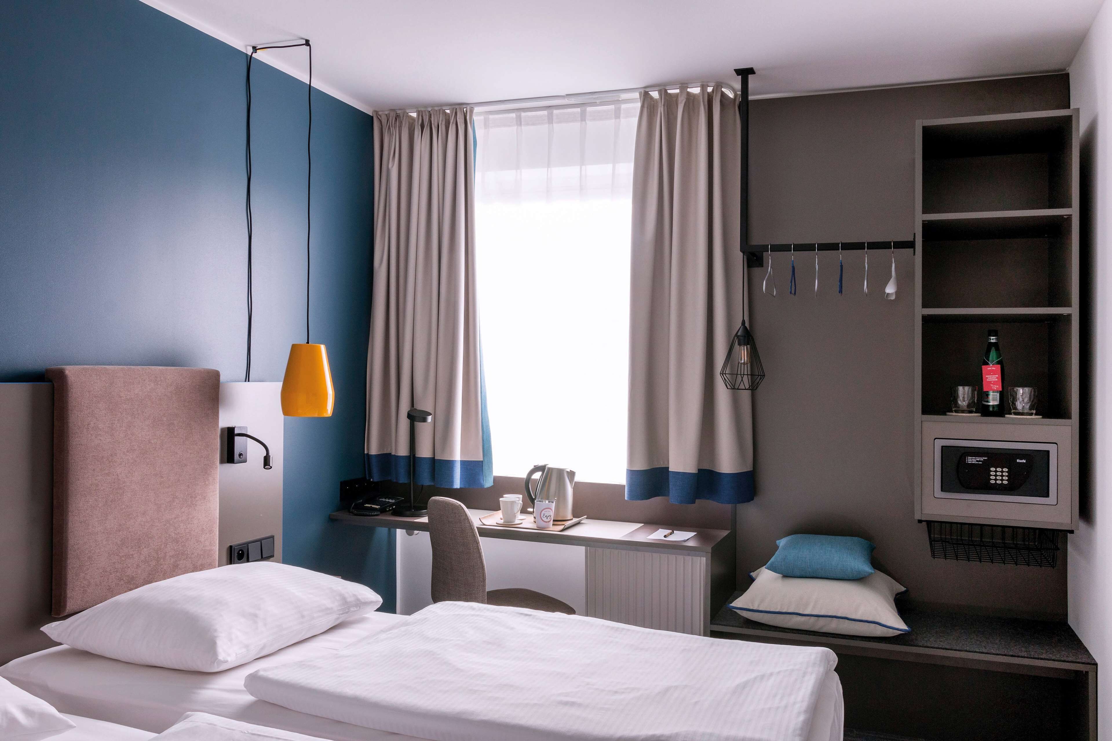 Habitació d'hotel amb llit, escriptori, cadira, microones i una estant amb ampolla i vasos.