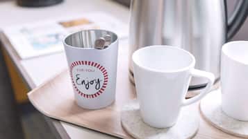 Una bandeja con una cafetera de acero inoxidable, una taza blanca con diseño rojo y blanco, y otra taza blanca sobre un posavasos.