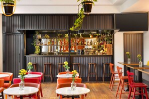 A modern bar area with a wooden bar counter, multiple stools, and tables with vases of yellow flowers. - Vienna House Easy by Wyndham Cracow (Kraków)
