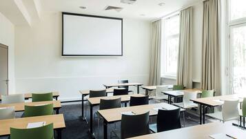 Un aula con escritorios y sillas dispuestas en filas, una pantalla de proyección grande en la pared y ventanas con cortinas.