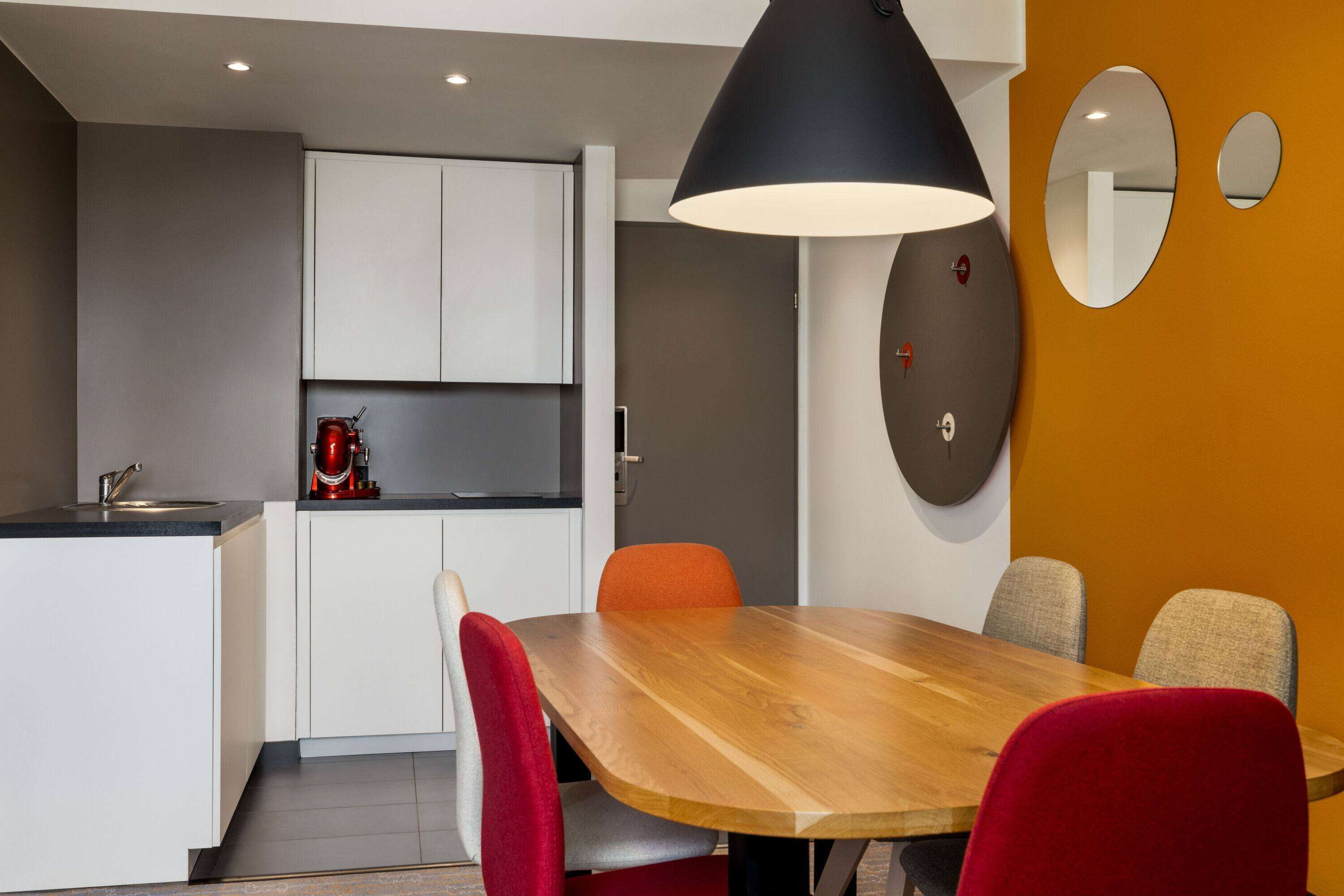 A modern kitchen with white cabinets, a wooden dining table, and red chairs.